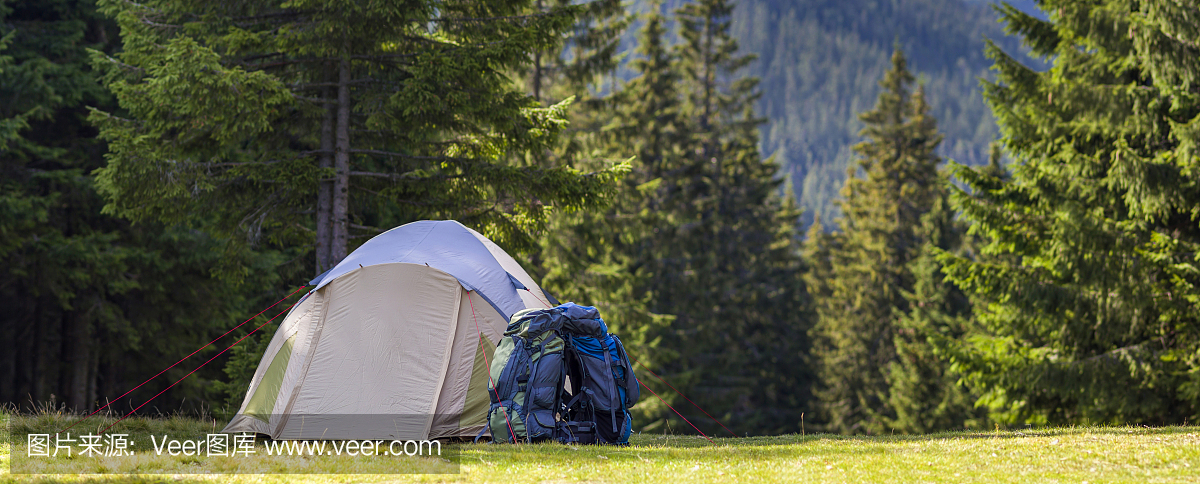 游客在喀尔巴阡山森林里的绿色草地上露营。徒步旅行者在露营地点搭帐篷和背包。积极的生活方式,户外活动,度假,运动和娱乐的概念。
